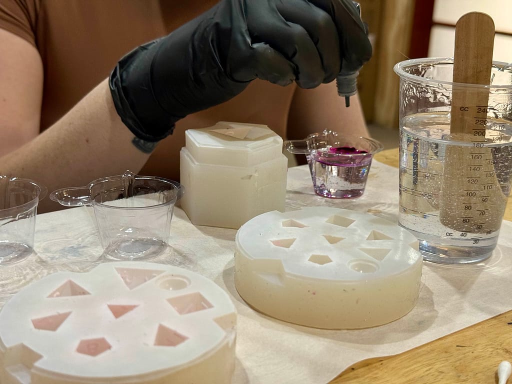 Woman dropping purple ink into resin ready to pour into a dice mould