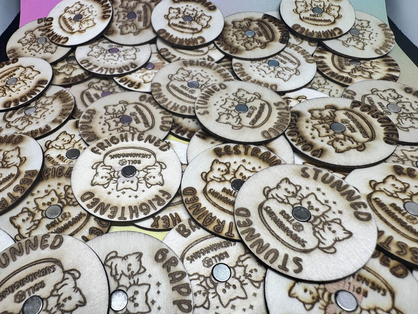 “Wooden laser-engraved magnetized condition marker rings from Roll 4 Shenanigans, featuring various TTRPG conditions like Frightened, Stunned, Grappled, and Restrained, displayed in a scattered group.”