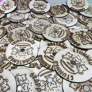 “Wooden laser-engraved magnetized condition marker rings from Roll 4 Shenanigans, featuring various TTRPG conditions like Frightened, Stunned, Grappled, and Restrained, displayed in a scattered group.”