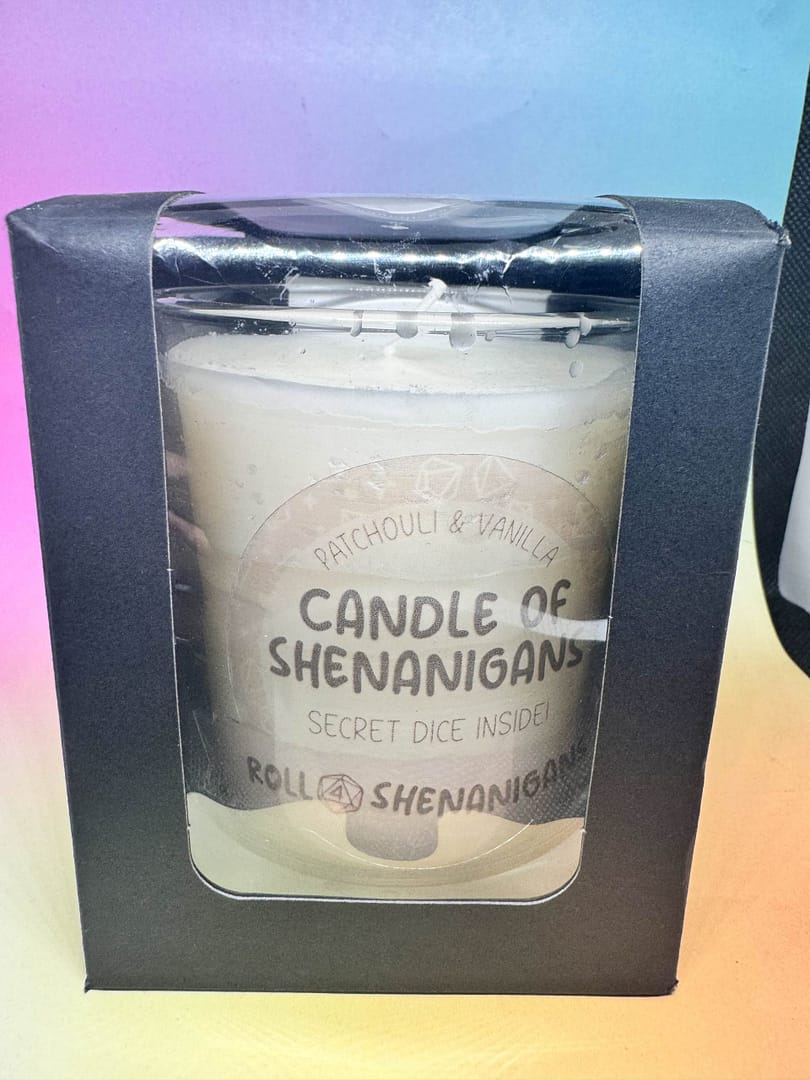 “Candle of Shenanigans Patchouli and Vanilla scented candle with secret mystery dice inside, made by Roll 4 Shenanigans, displayed against a pastel gradient background.”